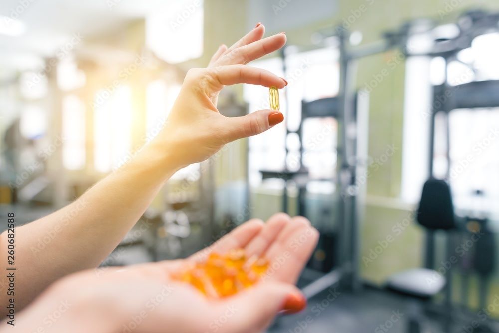 A woman holds a palmful of softgels in a gym. 